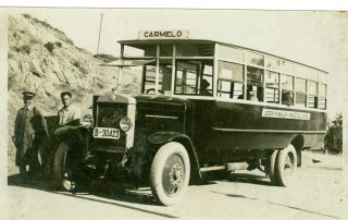 Fotografia antiga en color sèpia d'un autobús aturat amb el conductor i els passatgers a dins
