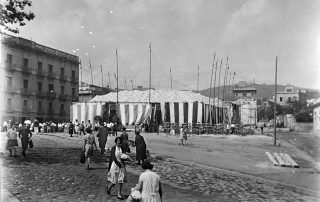 Fotografia antiga en blanc i negre d'un envelat a Gràcia amb vianants als anys 20