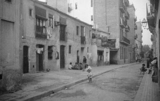 Fotografia antiga en blanc i negre d'un carrer amb els seus veïns