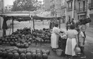 Fotografia antiga en blanc i negre d'una parada de melons en plena activitat de venda