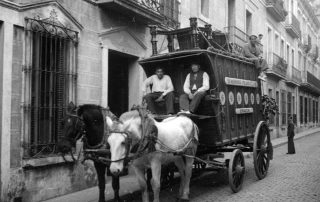 Fotografia antiga en blanc i negre d'un carruatge parat a un carrer amb els seus conductors