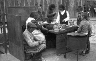 Fotografia antiga en blanc i negre d'una parada d'aliments amb els venedors i els clients