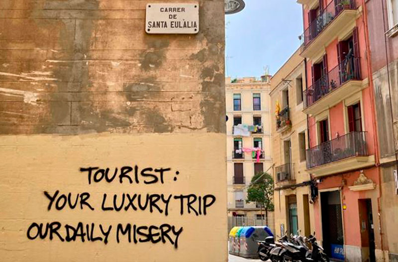 Fotografia a color d'un carrer del barri de Gràcia amb una pintada a la paret contra el turisme